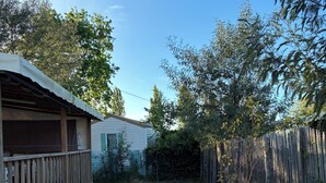 A backyard with a wooden deck, a fenced area, and a house in the background. - Fully equipped mobile home for 4–6 people in Hourtin, between the lake, the forest, and the ocean🏖️ (Hourtin)