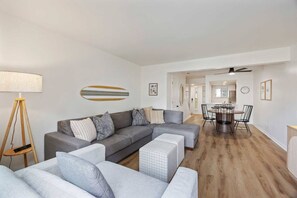 Ein modernes Wohnzimmer mit einer Eckcouch, einem Essbereich mit Tisch und Stühlen sowie einem Deckenventilator.