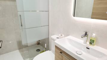 Ein modernes Badezimmer mit Duschkabine aus Glas, einer weißen Toilette und einem Waschbecken mit Spiegel.