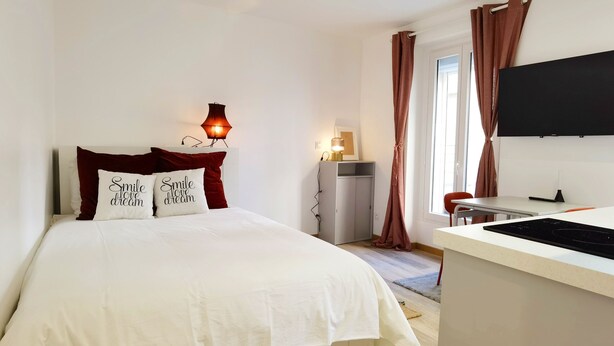 Een slaapkamer met een bed, een bedlamp, een televisie en een bureau met een stoel.