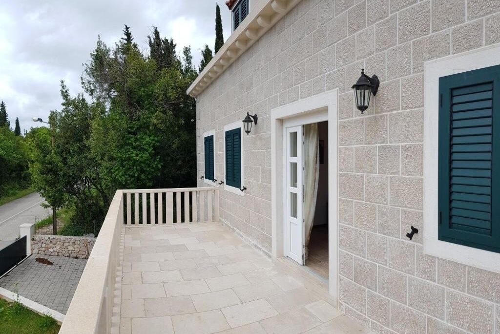 A building with a stone facade, green shutters, and a paved balcony area.