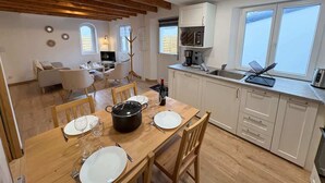 A modern kitchen with wooden beams, white cabinets, and a dining area with a table set for four. - New - small cosy cottage for 4 near the sea (Landunvez)