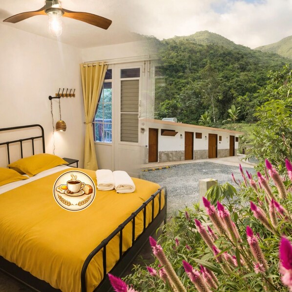 Una habitación con cama, ventilador de techo, ventana con cortinas y vistas a un paisaje montañoso.