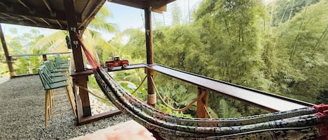 A hammock under a wooden structure with a view of lush greenery.