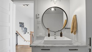 Ein modernes Badezimmer mit einem weißen Waschtisch, einem runden Spiegel und einem Handtuchhalter.