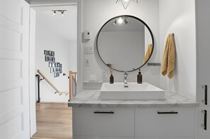 Ein modernes Badezimmer mit einem weißen Waschtisch, einem runden Spiegel und einem Handtuchhalter.