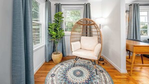 A room with a rattan chair, a patterned rug, and a potted plant. - Stylish Downtown Bungalow with Fire Pit (Carrboro)