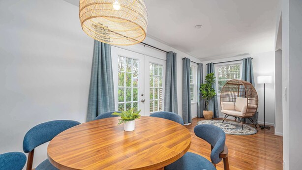 A dining area with a round wooden table, blue upholstered chairs, a wicker hanging light fixture, and a rattan chair. - Stylish Downtown Bungalow with Fire Pit (Carrboro)