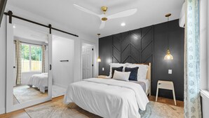 Ein modernes Schlafzimmer mit einem Bett, einem Deckenventilator und einem kleinen Hocker.