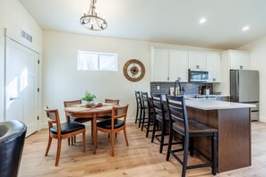 Une cuisine moderne avec des meubles blancs, un îlot central et un coin repas doté de chaises en bois.