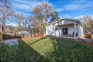 Ein bungalow mit überdachter Veranda, umzäunter Garten und blauem Himmel.