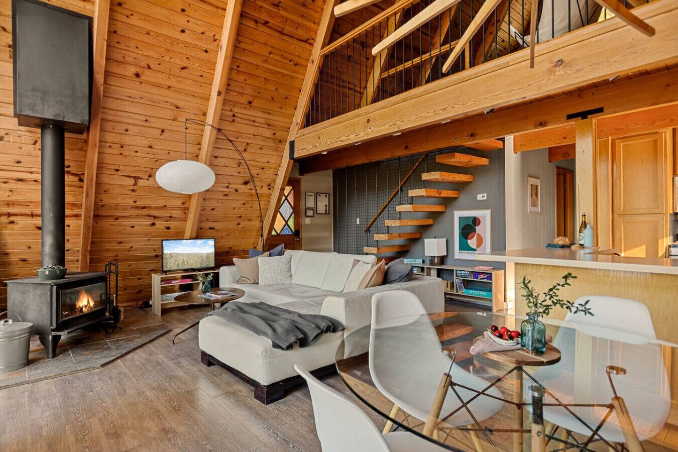 A cozy log cabin interior with a fireplace, a sofa, a dining table, and a staircase.