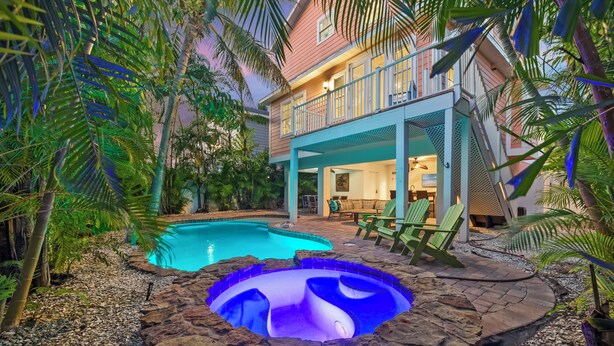 Ett hus med en swimmingpool och ett bubbelbad, omgivet av tropiska växter.