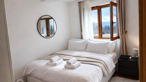 Ein Schlafzimmer mit einem Bett, einem runden Spiegel, einem Fenster mit Vorhängen und einem Nachttisch mit einer Lampe.