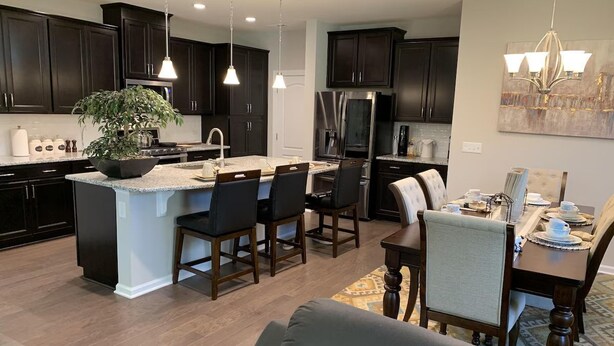 Una cocina moderna con armarios oscuros, una isla central, taburetes de bar y una mesa de comedor preparada para cuatro.