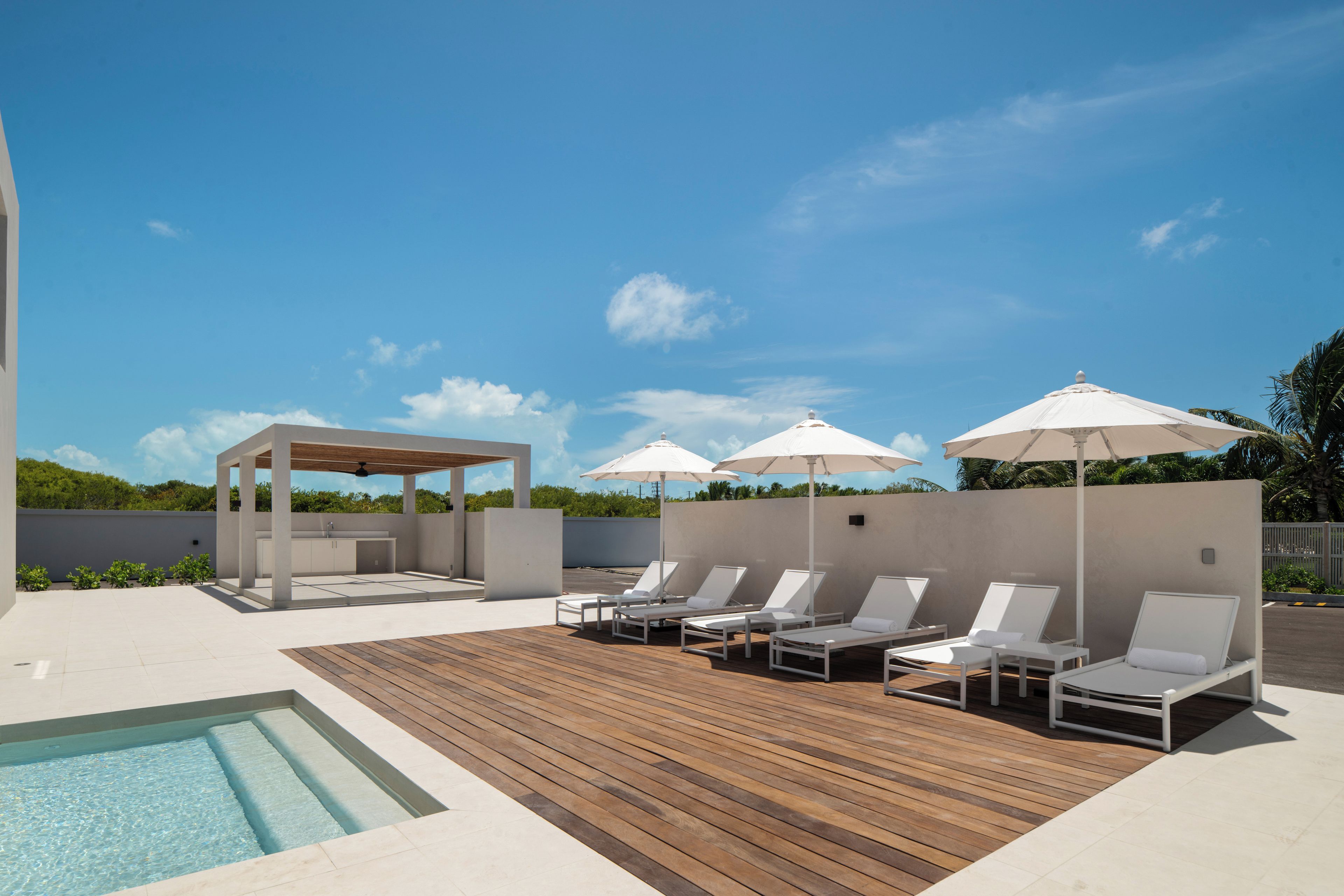 Uma área de piscina no terraço com espreguiçadeiras e guarda-sóis, um deck de madeira e uma piscina pequena.