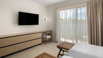 Una habitación de hotel con cama, escritorio, televisor y un ventanal con cortinas.