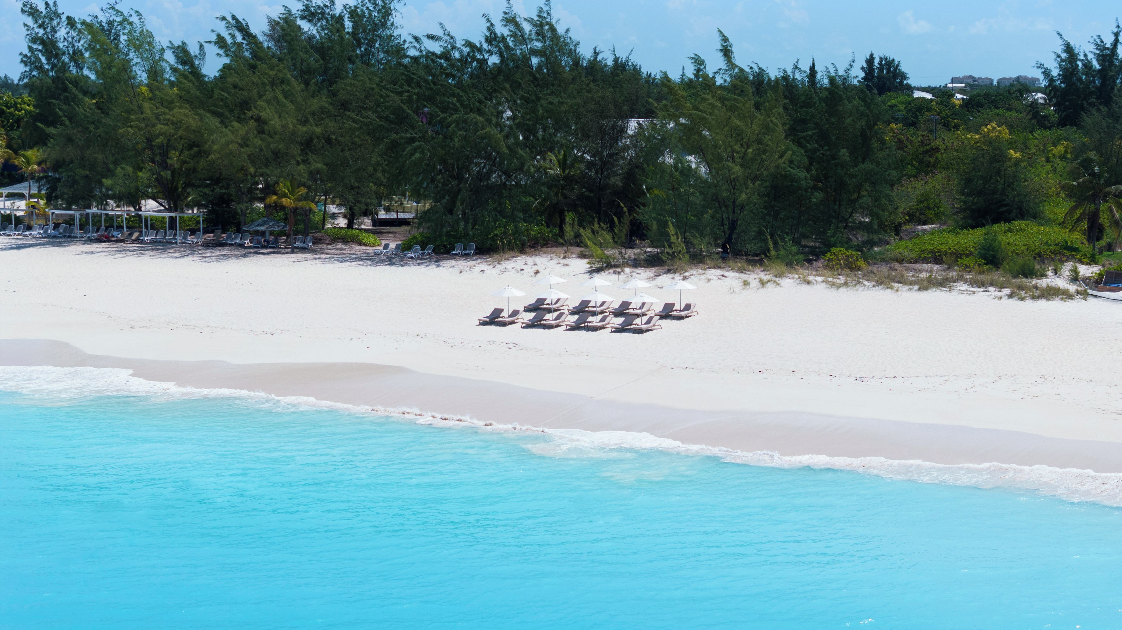 A beach with white sand, clear turquoise water, and rows of sun loungers.