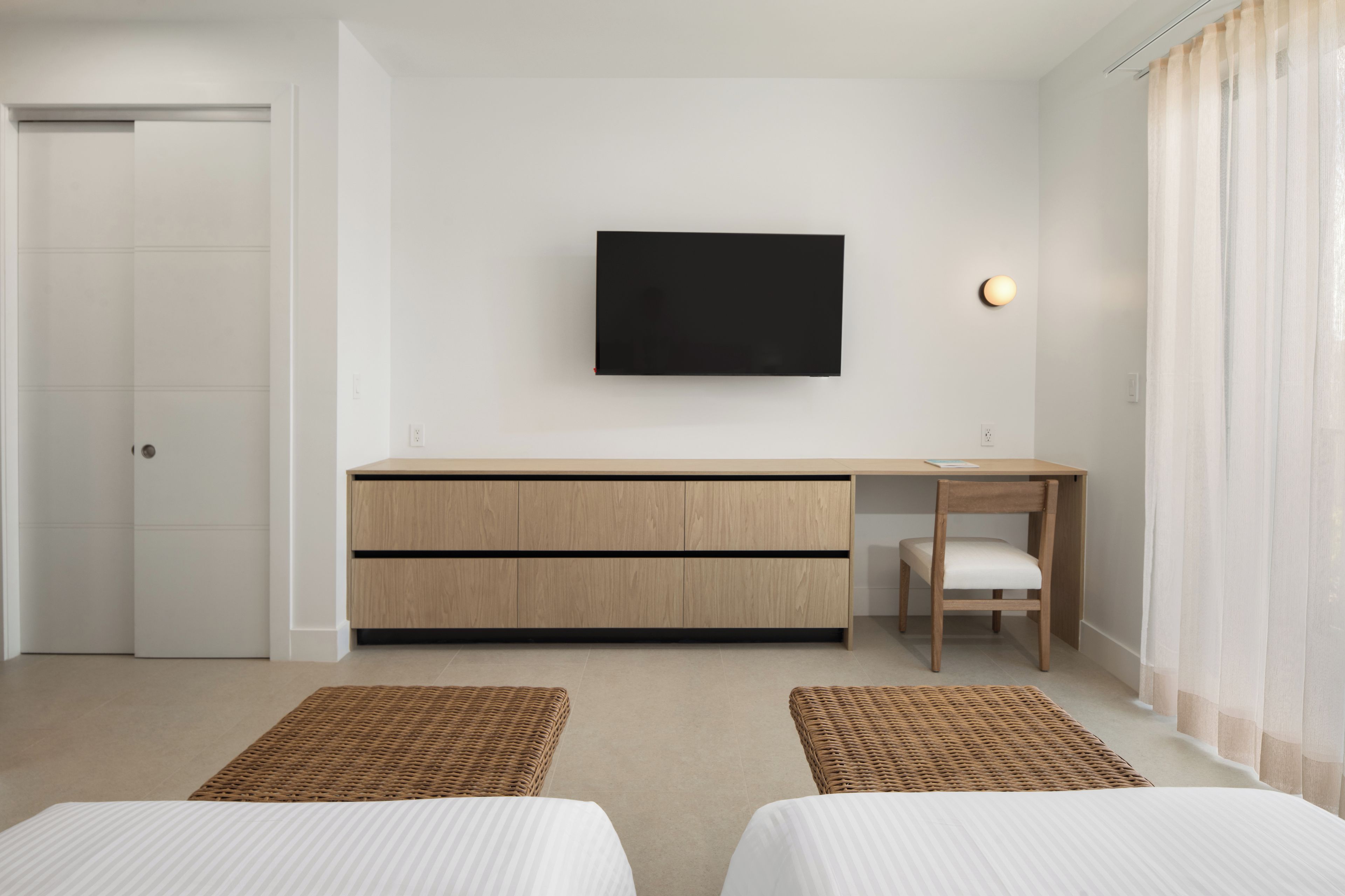 Una habitación de hotel moderna con una cama, un escritorio, una silla, un televisor y una puerta.