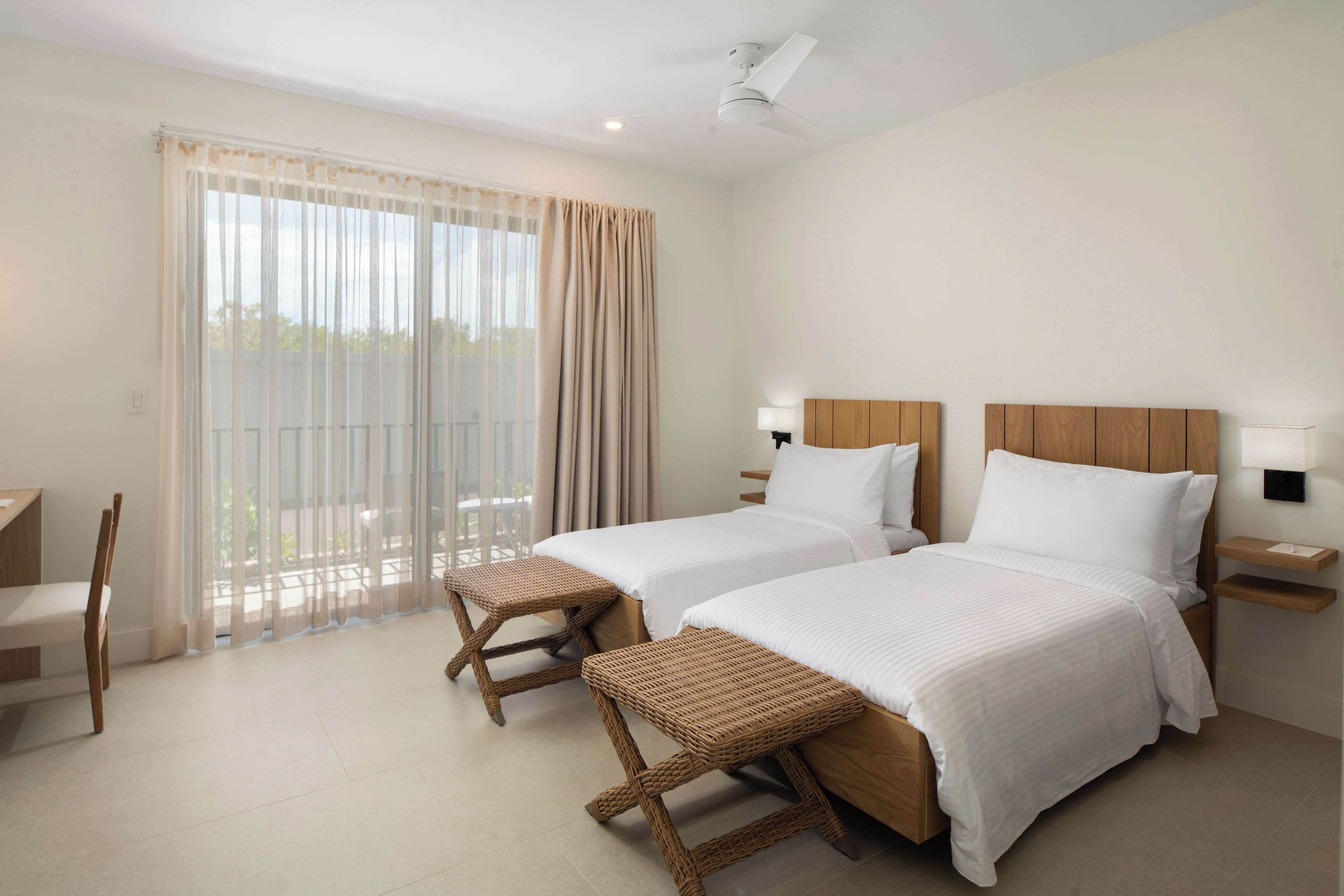 Ein Hotelzimmer mit zwei Betten, einem Balkon mit Vorhängen, einem Sessel und einem kleinen Tisch.