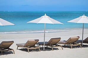Beach chairs and umbrellas arranged on a sandy beach with a view of the ocean. - The Retreat Turks & Caicos (Providenciales)