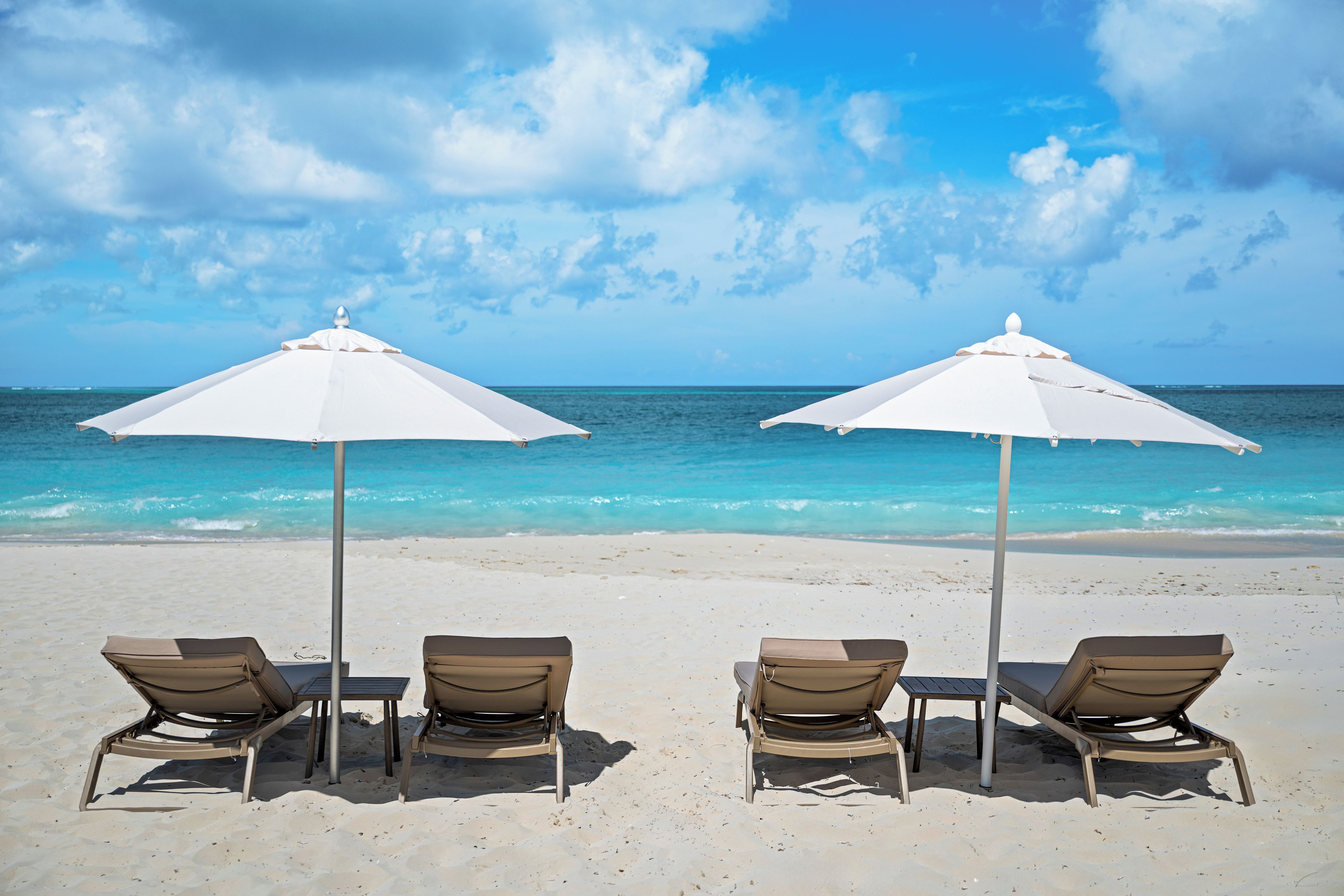 Vier strandstoelen met witte parasols op een zandstrand, gericht op de oceaan.