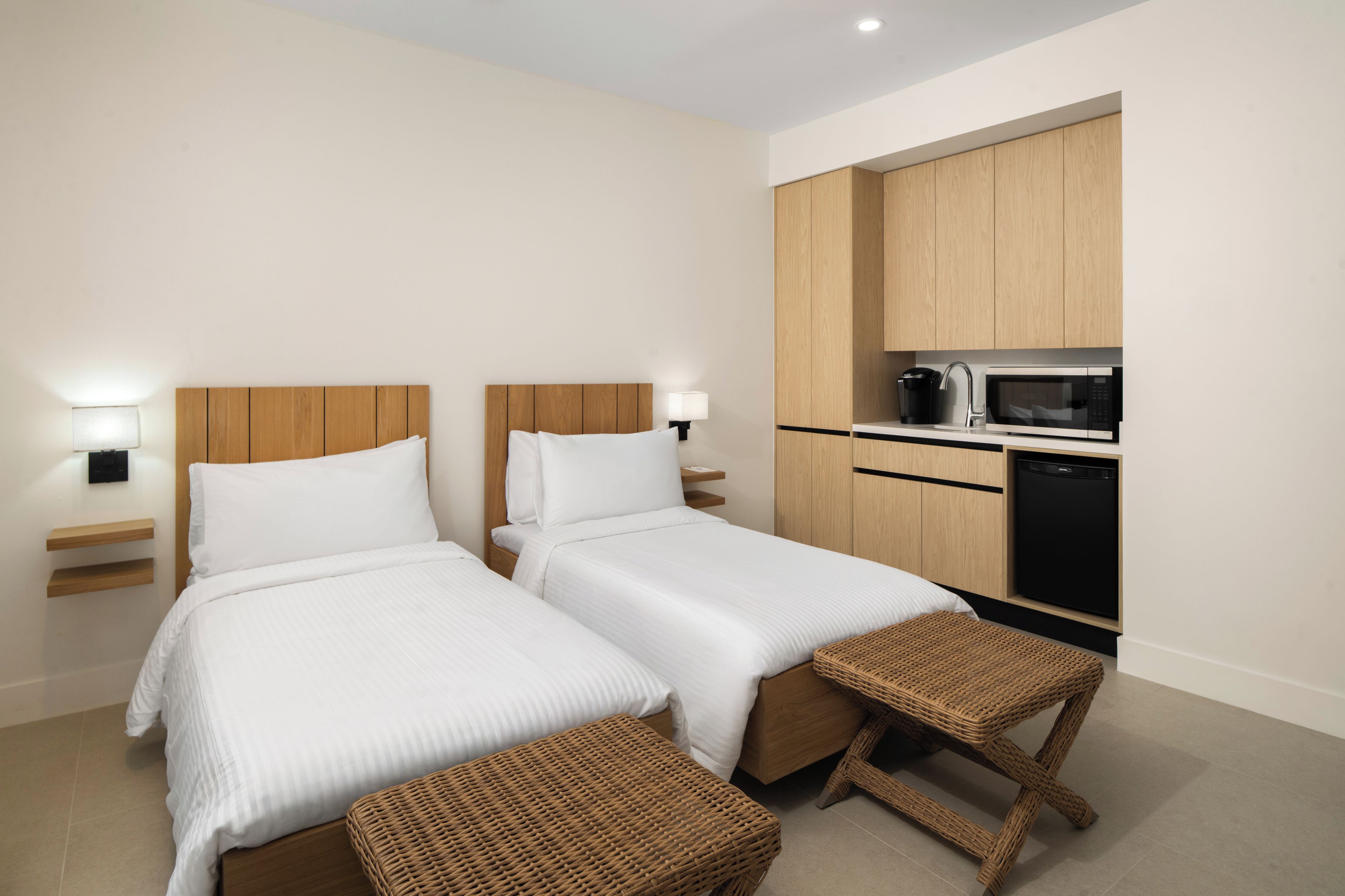 A hotel room with two beds, a kitchenette, and a small seating area.