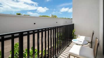 Ein Balkon mit einem weißen Tisch und Stühlen, einem schwarzen Metallgeländer und Blick auf Himmel und Grün.