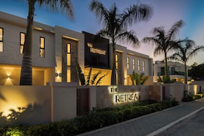 A modern building with a sign reading 'The Retreat.' It features a brick facade, large windows, and is surrounded by palm trees. - The Retreat Turks & Caicos (Providenciales)