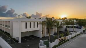 A modern building with a parking area, palm trees, and a sunset in the background. - The Retreat Turks & Caicos (Providenciales)