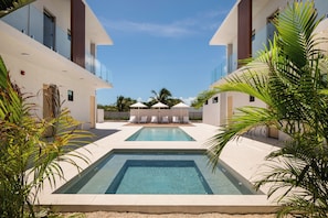 A modern pool area with clear blue water, surrounded by white buildings and palm trees.
