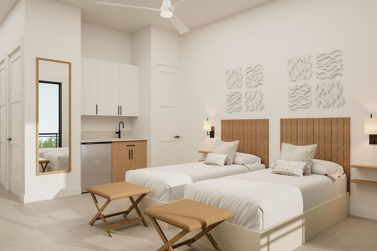 Een moderne slaapkamer met twee bedden, een klein kitchenette, een plafondventilator en een grote spiegel.