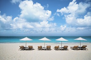 A beach with white umbrellas and lounge chairs facing the ocean. - The Retreat Turks & Caicos (Providenciales)