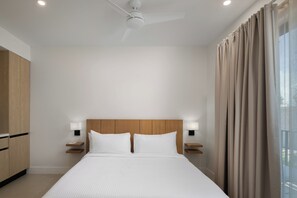 A hotel room with a large bed, wooden headboard, bedside lamps, and a ceiling fan. - The Retreat Turks & Caicos (Providenciales)