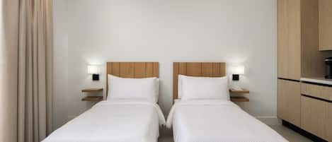 A hotel room with two single beds, bedside tables with lamps, a wooden wardrobe, and a large window with curtains.