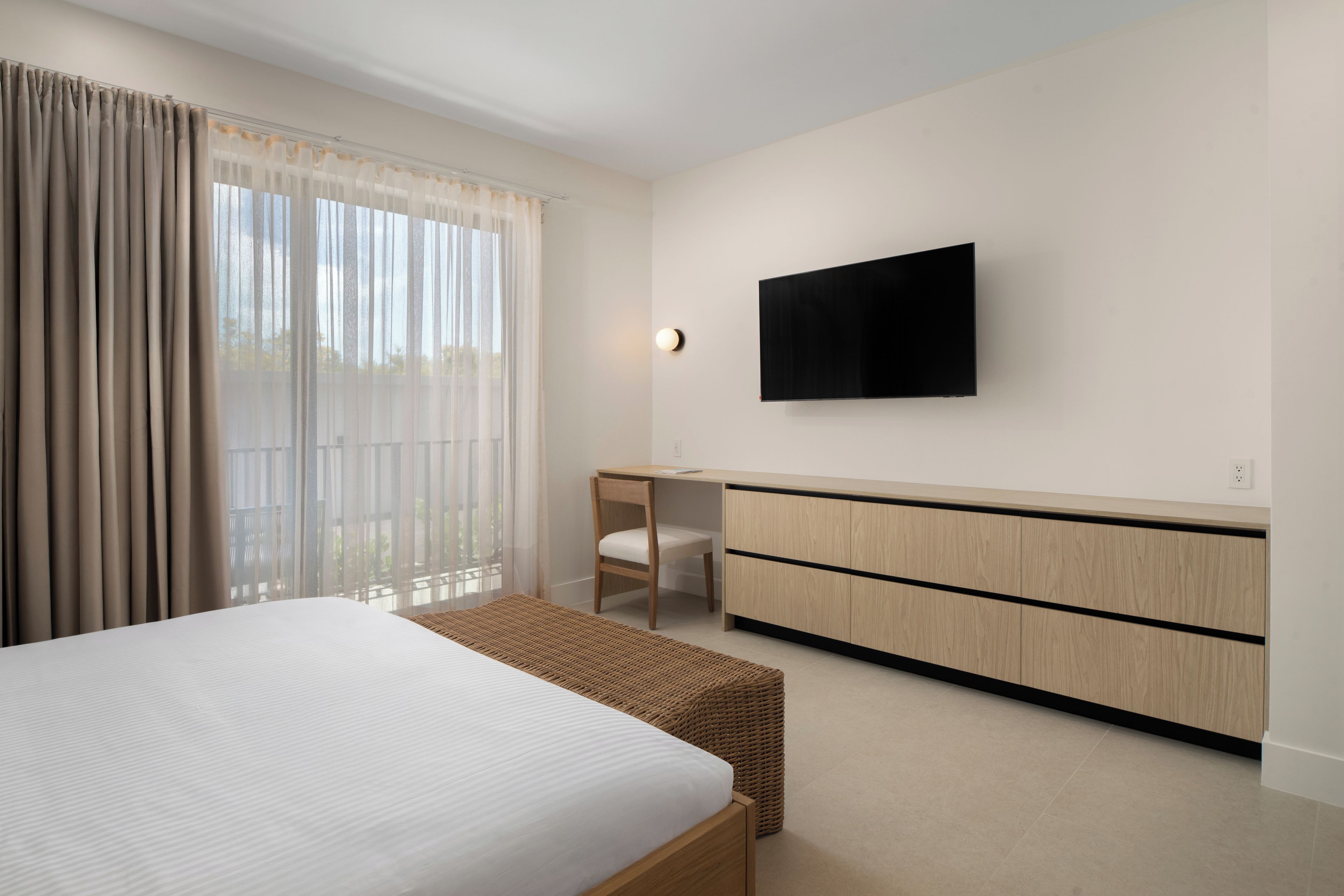 A modern hotel room with a large bed, a desk, a television, and a view of the outdoors.