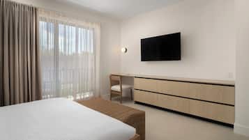 A modern hotel room with a large bed, a desk, a television, and a view of the outdoors.