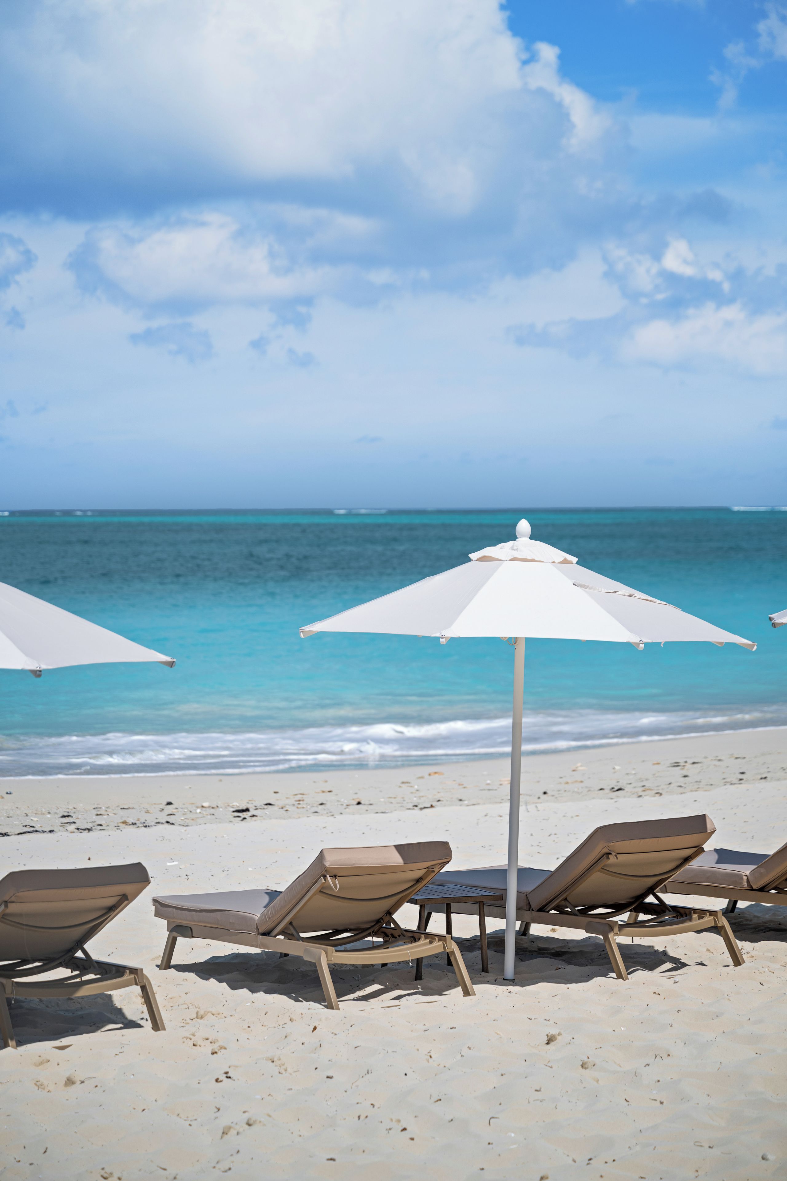 A beach with white umbrellas and brown lounge chairs.