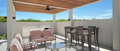 Een terras buiten met een plafondventilator, een bank, een tafel en stoelen.