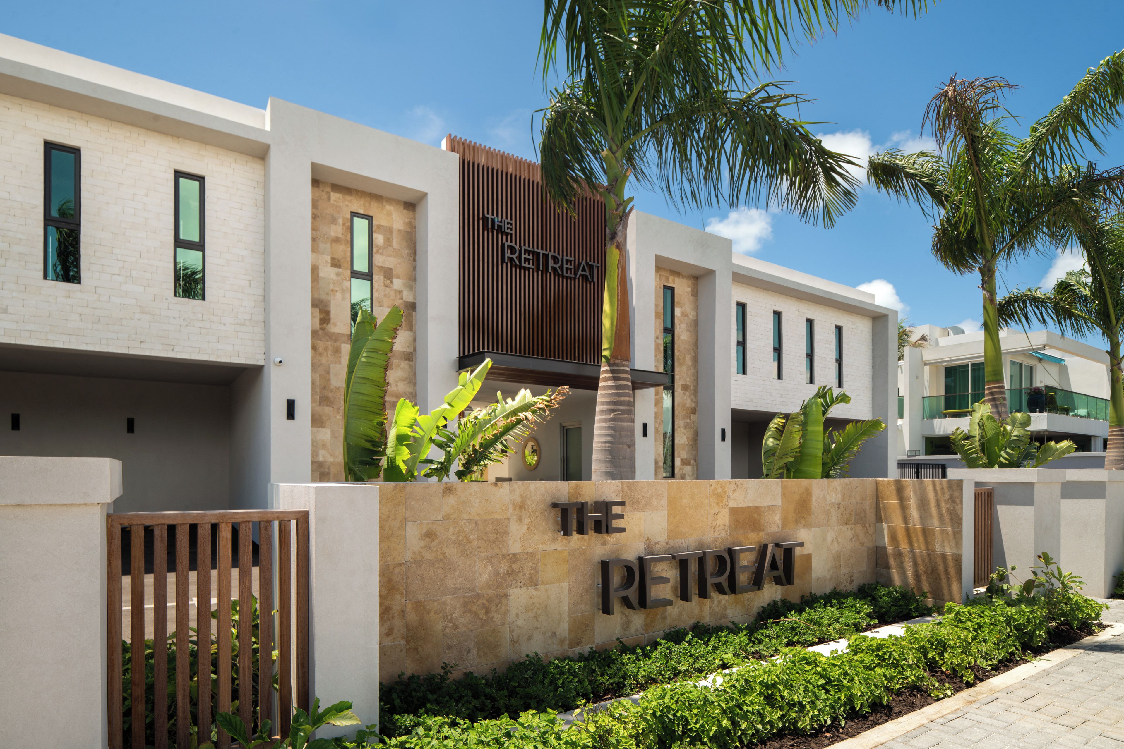 Un edificio moderno con un letrero que dice 'The Retreat'. Presenta una combinación de fachadas de ladrillo y piedra, grandes ventanales y un jardín bien cuidado con diversas plantas.