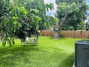 Ein Garten mit Rasenfläche, einem Baum, einem Zaun und Gartenmöbeln.