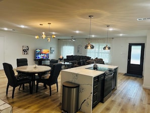 Eine moderne Küche mit Kochinsel, Essbereich mit Stühlen, einem Fernseher und einer Couch.