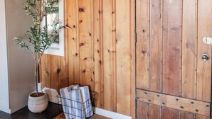 Een houten interieur met een deur, een potplant, een ingelijste foto en een deurmat.