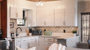 Een moderne keuken met witte kastjes, een magnetron en een broodrooster. Er is een raam met uitzicht op het exterieur.