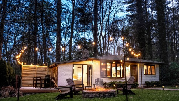 Een klein huis met een terras, buitenmeubels en een vuurkorf.