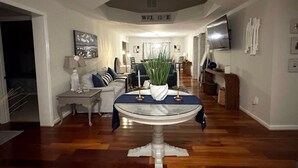 A modern living room with a round glass table, a sofa, and a television mounted on the wall. - Lighthouse Cottage | Ocean Pines, Golf & OC Beach (Ocean Pines)