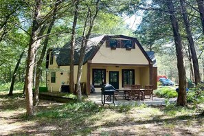 Une maison à deux étages avec un porche, entourée d’arbres.
