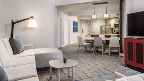 Ett modernt hotellrum med en soffa, ett litet bord, en TV och en matplats med stolar och ett bord.