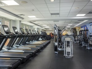 Ein Fitnessstudio mit mehreren in Reihen angeordneten Laufbändern, Krafttrainingsgeräten und einer Spiegelwand.