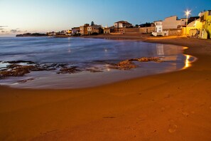 Una playa con mar tranquilo, orilla arenosa y edificios al fondo.